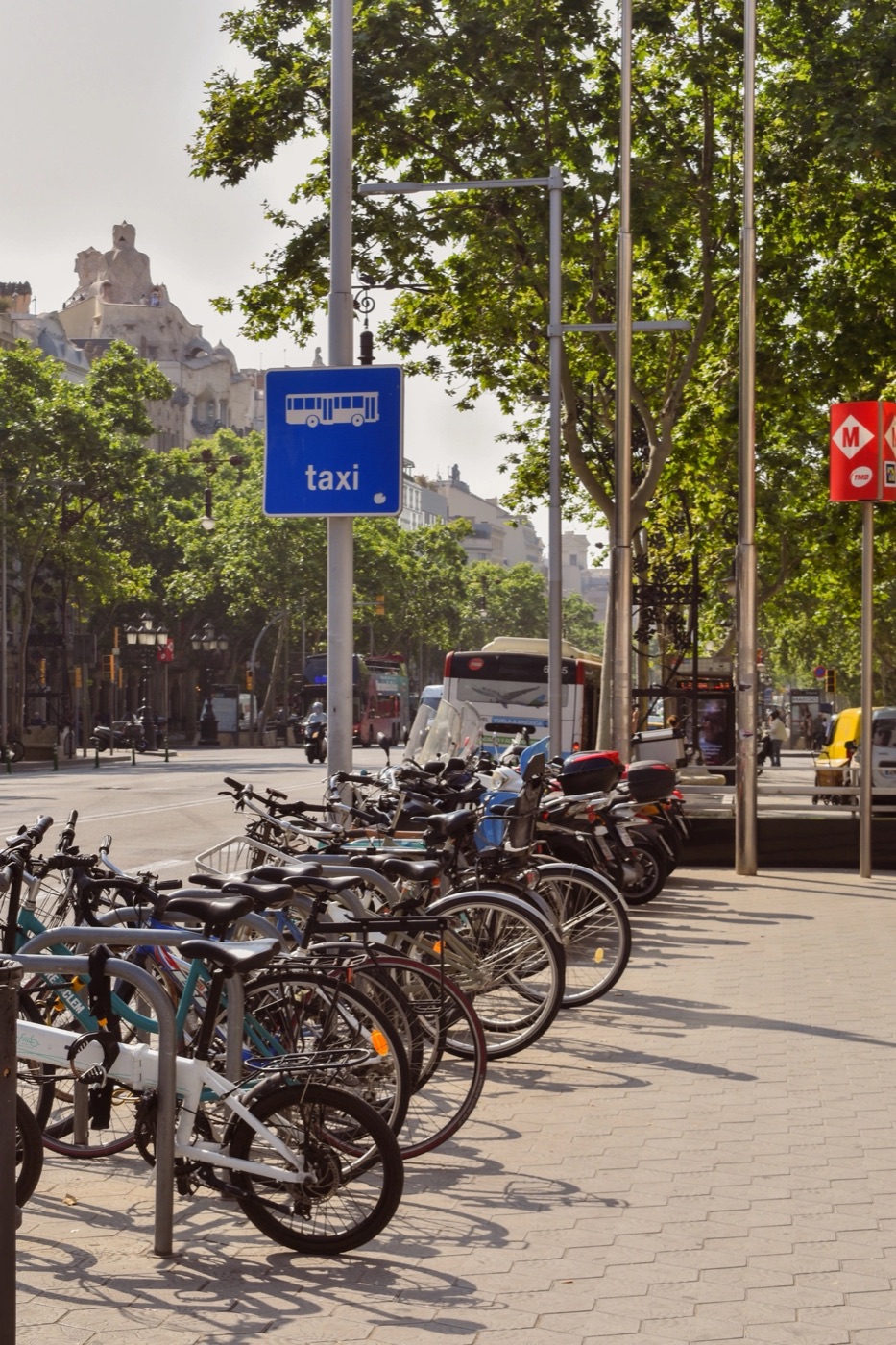 Privately owned bicycles locked in a row along a Barcelona avenue, next to bus and metro signs